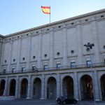 Edifício histórico da administração pública em Madrid, com a bandeira da Espanha no topo.
