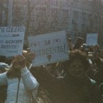 Grupo de estudantes participa de um protesto ao ar livre segurando cartazes.