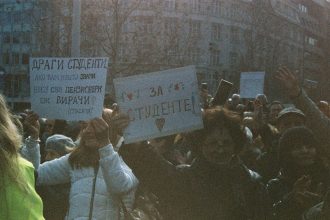 Grupo de estudantes participa de um protesto ao ar livre segurando cartazes.