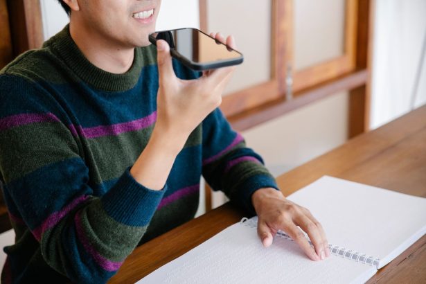 Homem sorrindo usa comandos de voz no celular sentado à mesa em casa.