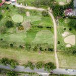 Vista aérea de um campo de golfe com greens, bunkers e caminhos cercados por árvores.
