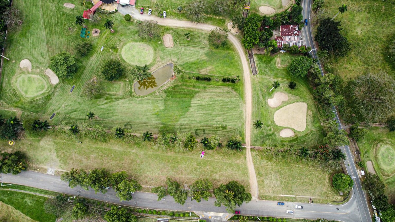 Vista aérea de um campo de golfe com greens, bunkers e caminhos cercados por árvores.