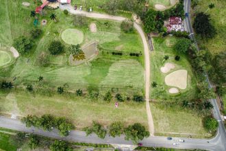 Vista aérea de um campo de golfe com greens, bunkers e caminhos cercados por árvores.