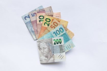 Cédulas de reais brasileiros dispostas em leque sobre fundo branco.