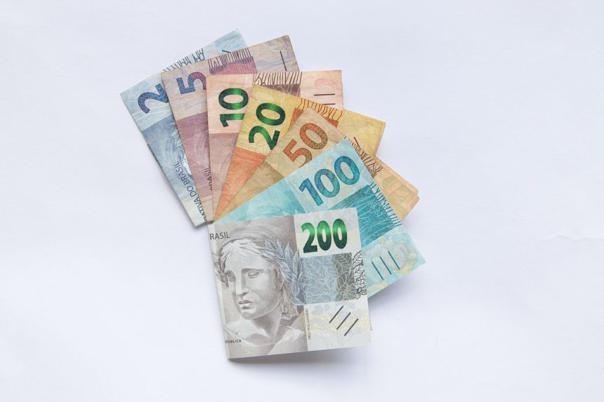Cédulas de reais brasileiros dispostas em leque sobre fundo branco.
